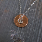 Penny with a saguaro cactus charm on a chain against a textured gray background