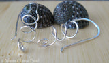 Silver spiral wire earrings on light wood with black shells