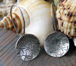 Silver disc starfish earrings on gray stone with white shell