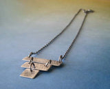 Silver strips pendant necklace shown on blue to tan gradient background