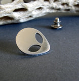 silver alien tie tack pin on gray with driftwood