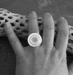 Silver sun ring on hand model resting on driftwood