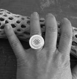 Silver sun ring on hand model resting on driftwood