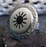 Silver sun round ring on rock with driftwood in background