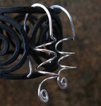 Hanging silver spiral earrngs with dark background and black spirals