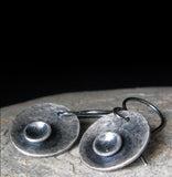 Silver disc earrings on gray stone with black background