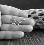 Silver dopamine molecule lapel pin held in hand with driftwood in black and white