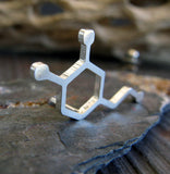 Silver dopamine molecule tie tack pin on gray rock