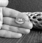 frog face tie tack held in  hand with driftwood