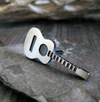Acoustic Guitar tie tack pin on gray stone with driftwood