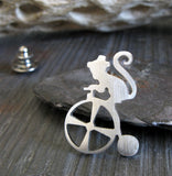 Silver Circus Monkey on Tricycle tie tack pin on dark background with driftwood