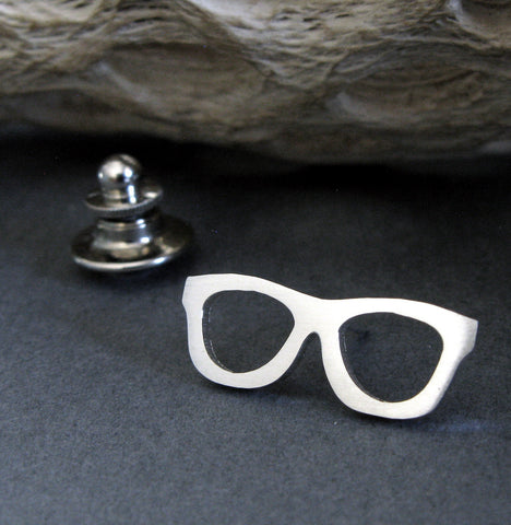 silver glasses tie tack pin on black background with driftwood