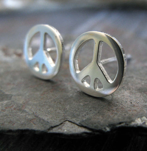 silver peace sign stud earrings on a gray rock