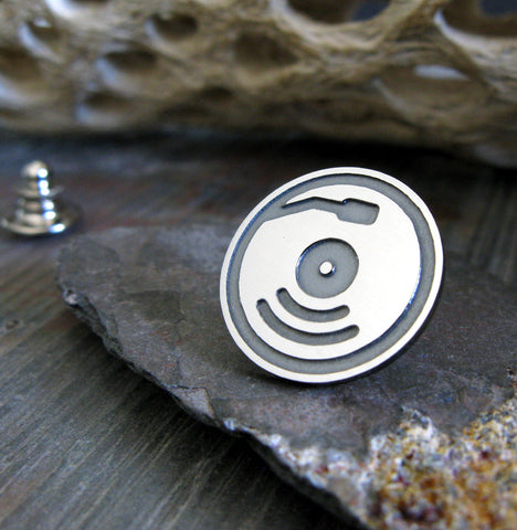 Silver and Black record pin on gray rock with driftwood