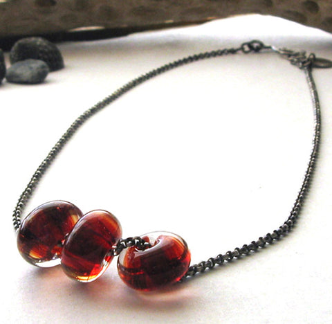 red glass beads on oxidized sterling silver chain white background with driftwood