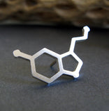 silver serotonin molecule tie tack on gray background with driftwood
