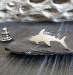 Silver shark tie tack pin sitting on gray rock with driftwood