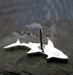 back side of silver shark lapel pin on gray rock