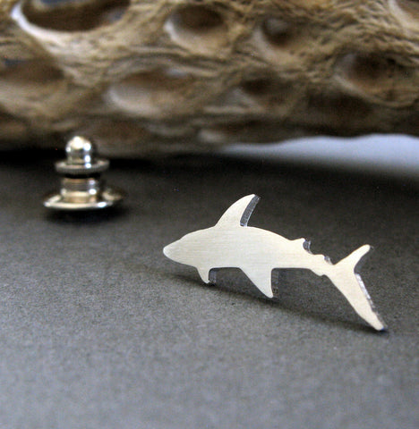 Silver tie tack shark pin shown on a dark background with driftwood