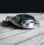 Dark blue Moss Agate pendant on wood grain with black horizon