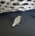 Silver Raven lapel pin sitting on black background with dirftwood