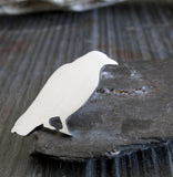 Silver Raven lapel pin sitting on gray stone