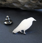 Silver Raven lapel pin sitting on black background with driftwood