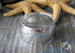 Sterling silver wide ring band laying on side with starfish in background