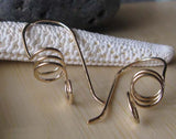 Gold spiral wire earrings on light wood with white starfish